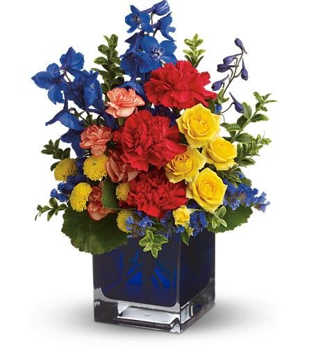 Bold colorful flower arrangement in a blue cube vase